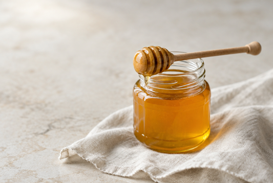 A honey dipper resting across a jar of golden honey