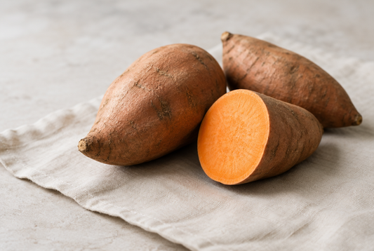 Two sweet potatoes, one cut to show orange flesh