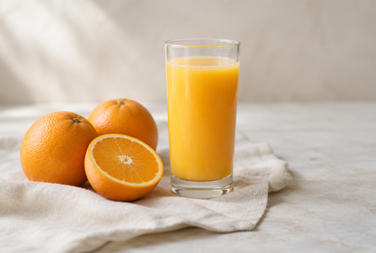 A glass of orange juice with whole oranges beside it